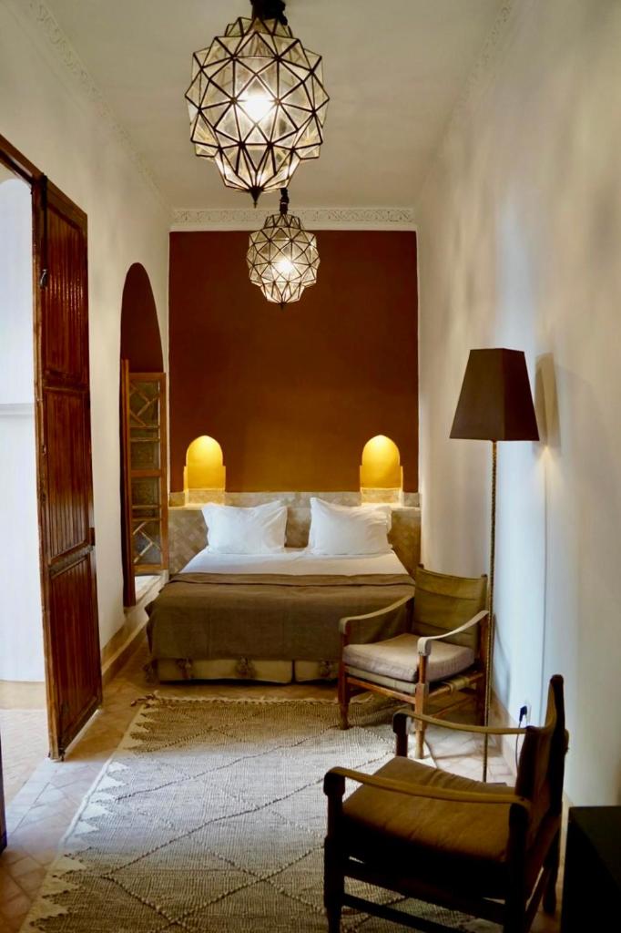 - une chambre avec un lit, une chaise et un lustre dans l'établissement Riad Tzarra, à Marrakech