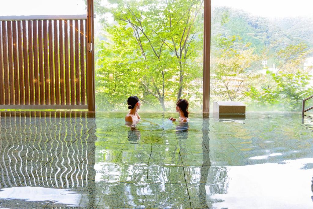 2 filles assises dans l'eau dans une piscine dans l'établissement Ooedo Onsen Monogatari Hotel Kinugawa Gyoen, à Nikkō