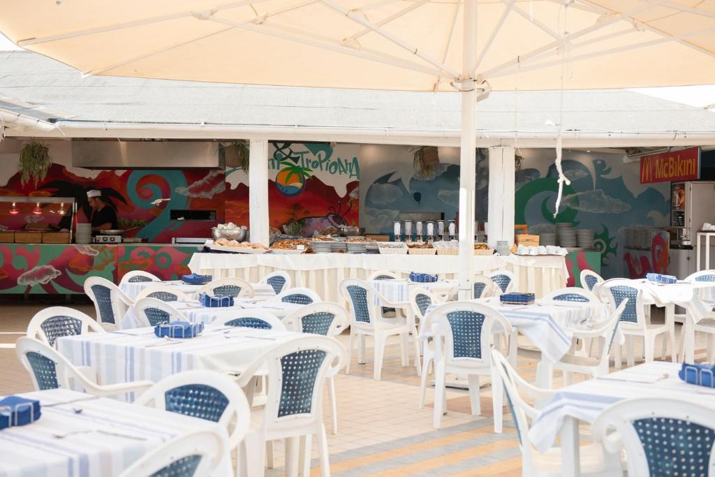 un restaurant avec des tables et des chaises blanches ainsi qu'un parasol dans l'établissement Bikini Tropicana Family Hotel, à Lido di Savio