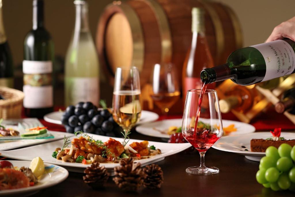 une personne versant du vin dans un verre sur une table avec de la nourriture dans l'établissement Ooedo Onsen Monogatari Hotel Shinko, à Fuefuki