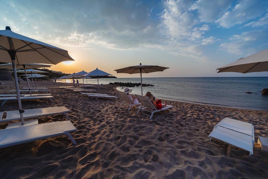 une personne assise sur une chaise longue sur une plage avec des parasols dans l'établissement Le Calette N.5, à Cefalù