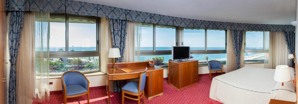 une chambre d'hôtel avec un lit, un bureau et des fenêtres dans l'établissement Hotel La Tonnara, à Amantea