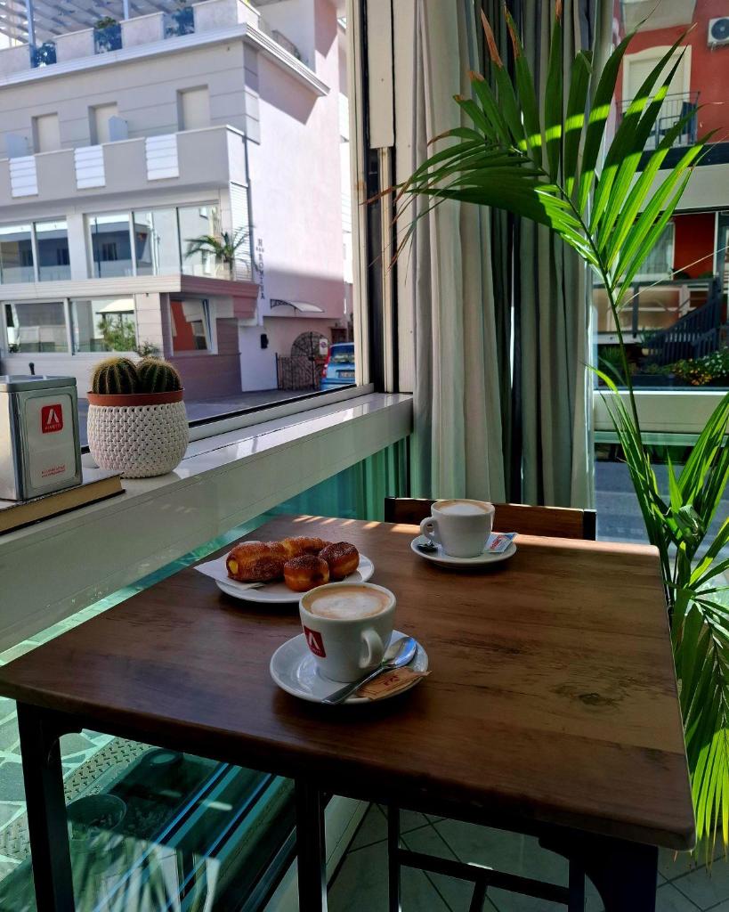 une table en bois avec deux tasses et des assiettes de nourriture dans l'établissement Hotel Brotas, à Rimini
