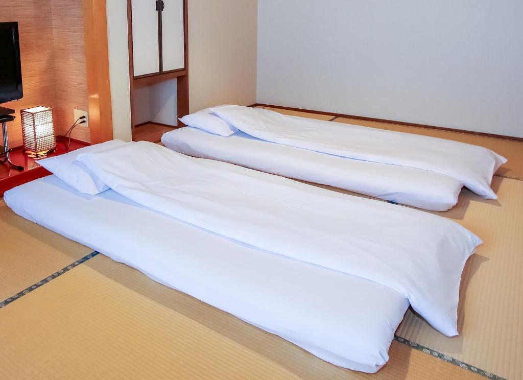 deux lits dans une chambre avec des draps blancs dans l'établissement 別府鉄輪温泉 萬力屋manrikiya, à Beppu