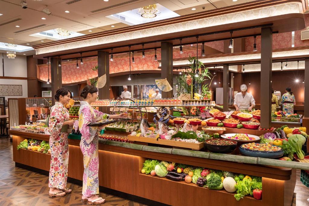 deux femmes en kimono debout devant un buffet dans l'établissement Ooedo Onsen Monogatari Amakusa Hotel Kameya, à Kami Amakusa