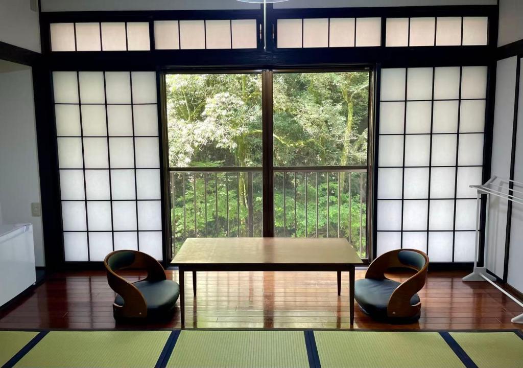 Cette chambre dispose d'une grande fenêtre, d'une table et de 2 chaises. dans l'établissement 天然温泉旅館 繁花荘せせらぎ, à Kirishima 45 autres photos