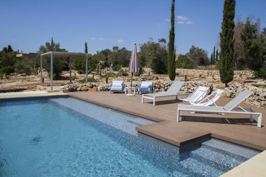 - une piscine avec des chaises longues blanches et un parasol dans l'établissement Villa Platino, à Torre Vado