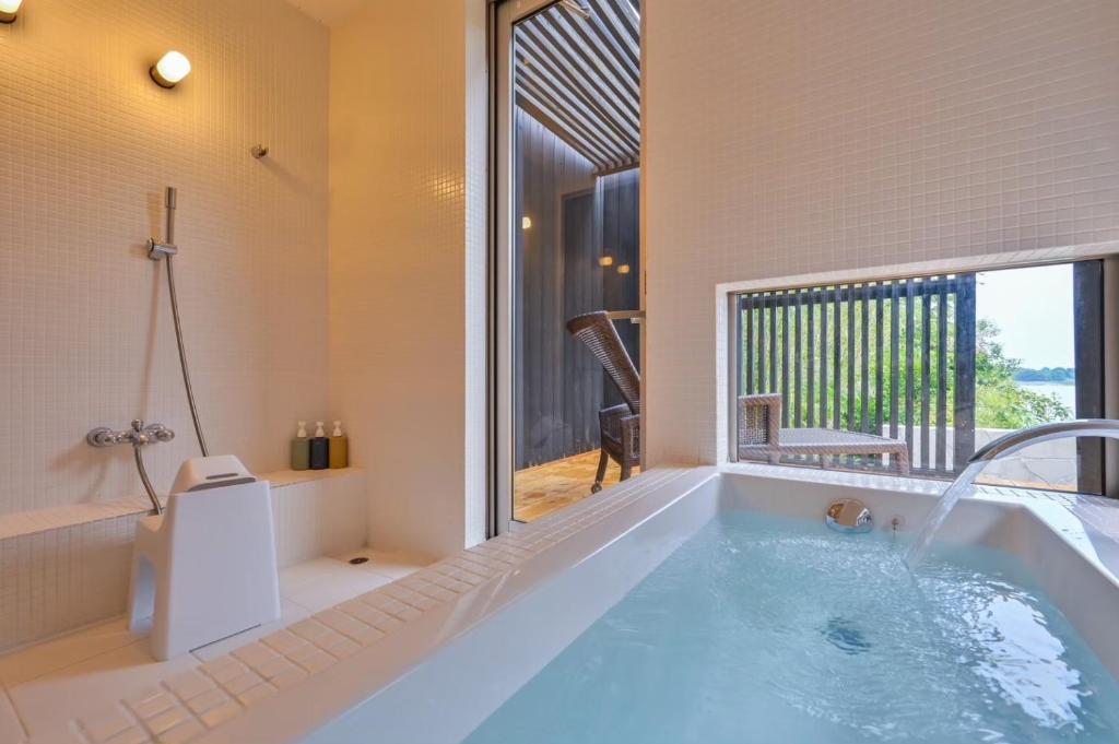 une baignoire dans une salle de bain avec une grande fenêtre dans l'établissement Tara Dakeonsen Kanigoten, à Tara