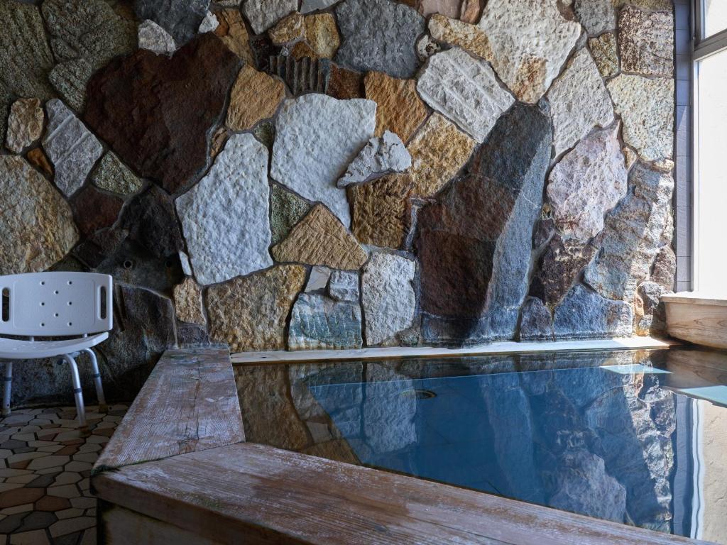 un mur de pierre avec une piscine dans une pièce avec une chaise dans l'établissement Donkairo, à Ako