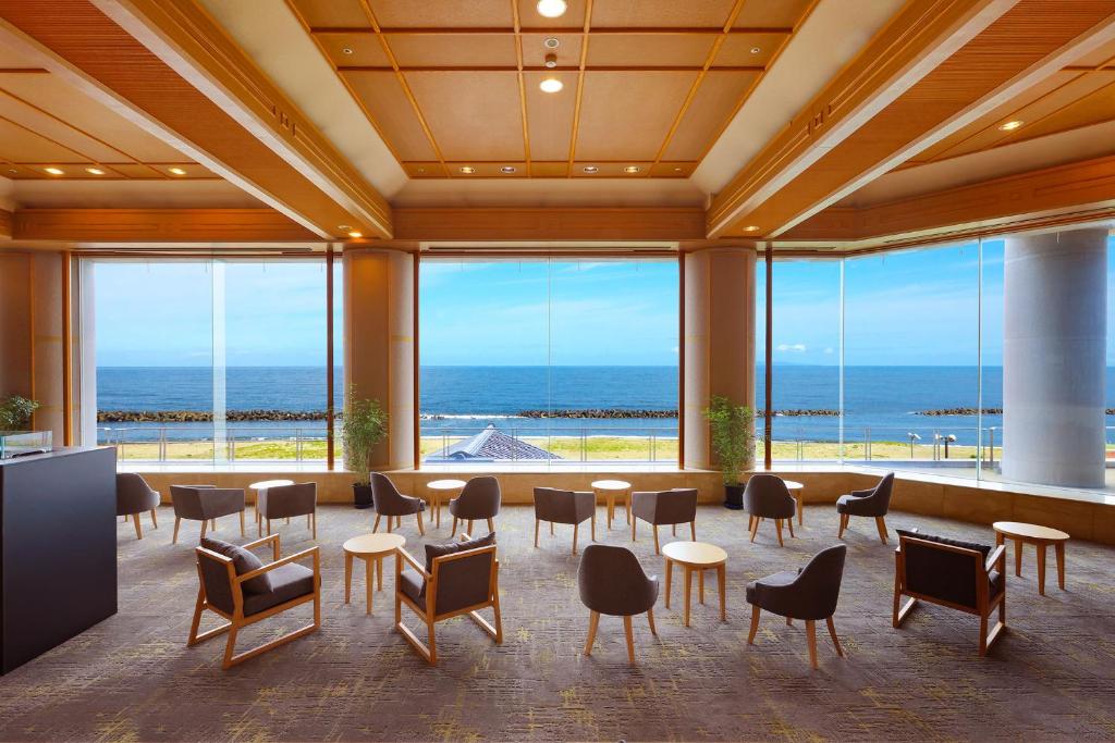 une grande chambre avec des tables et des chaises et l'océan dans l'établissement Ooedo Onsen Monogatari Premium Shiomiso, à Murakami