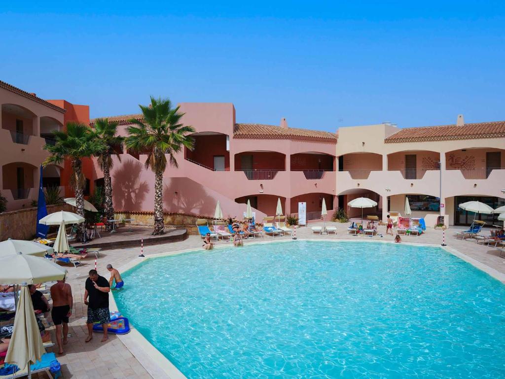 une piscine dans un complexe hôtelier avec des gens debout autour dans l'établissement Red Sun Village, à Isola Rossa