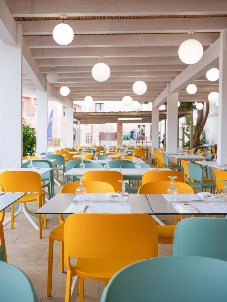 une salle à manger vide avec des tables et des chaises jaunes dans l'établissement Red Sun Village, à Isola Rossa