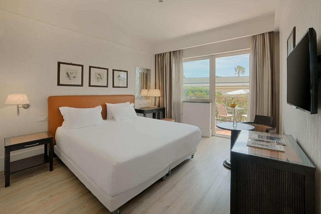 une chambre avec un grand lit blanc et une télévision dans l'établissement NH Catania Parco degli Aragonesi, à Catane