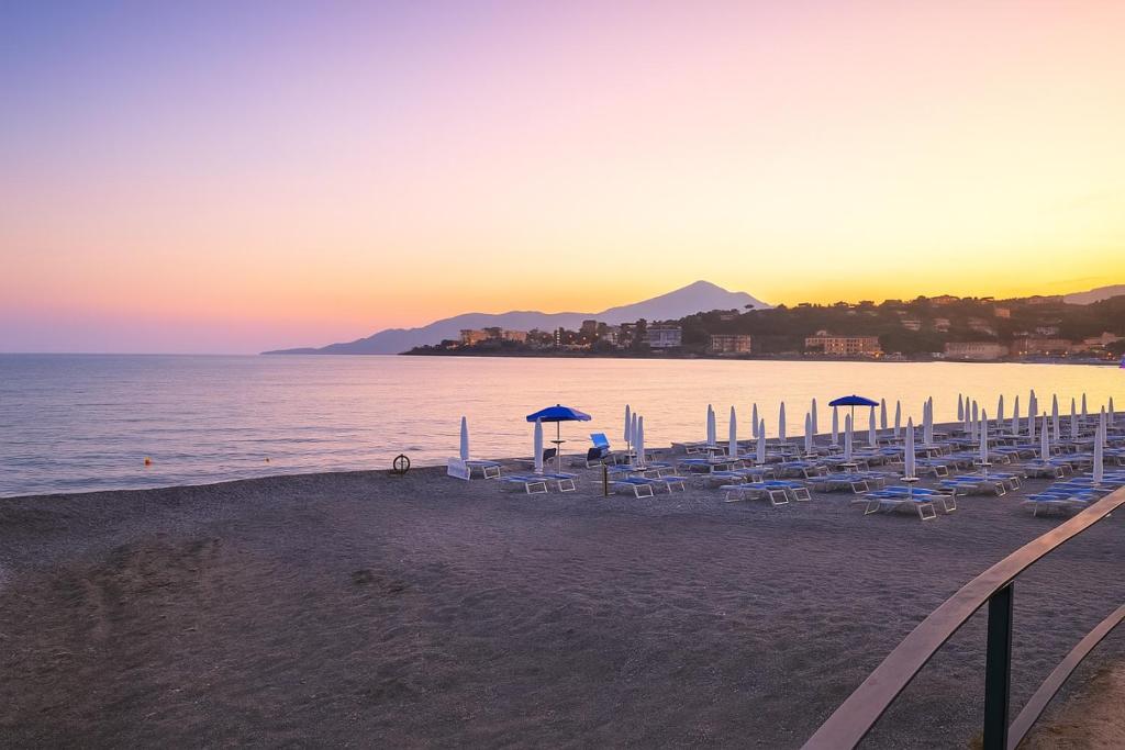 - une plage avec des chaises et des parasols au coucher du soleil dans l'établissement Hotel Poseidonia, à Sapri
