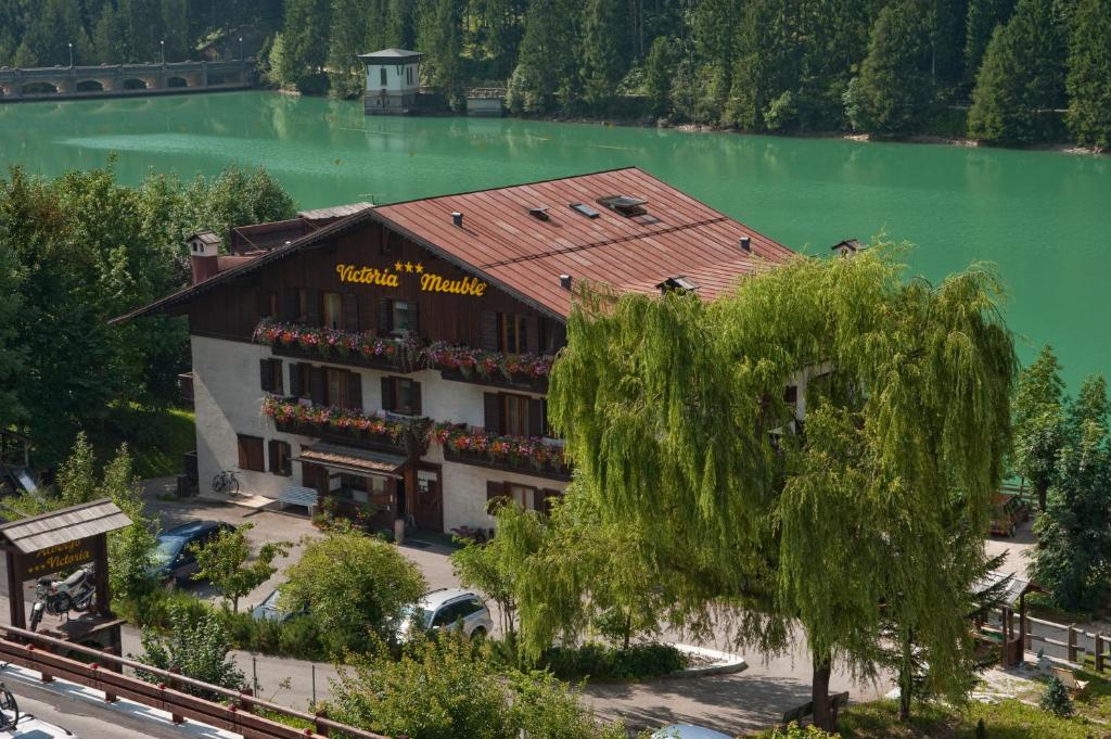un bâtiment à côté d'un lac avec un arbre dans l'établissement Albergo Meublè Victoria, à Auronzo di Cadore