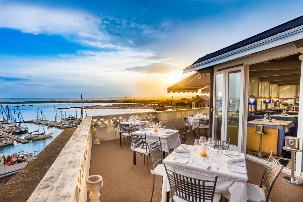 un restaurant avec des tables et des chaises sur un balcon dans l'établissement Grand Hotel Ortigia, à Syracuse