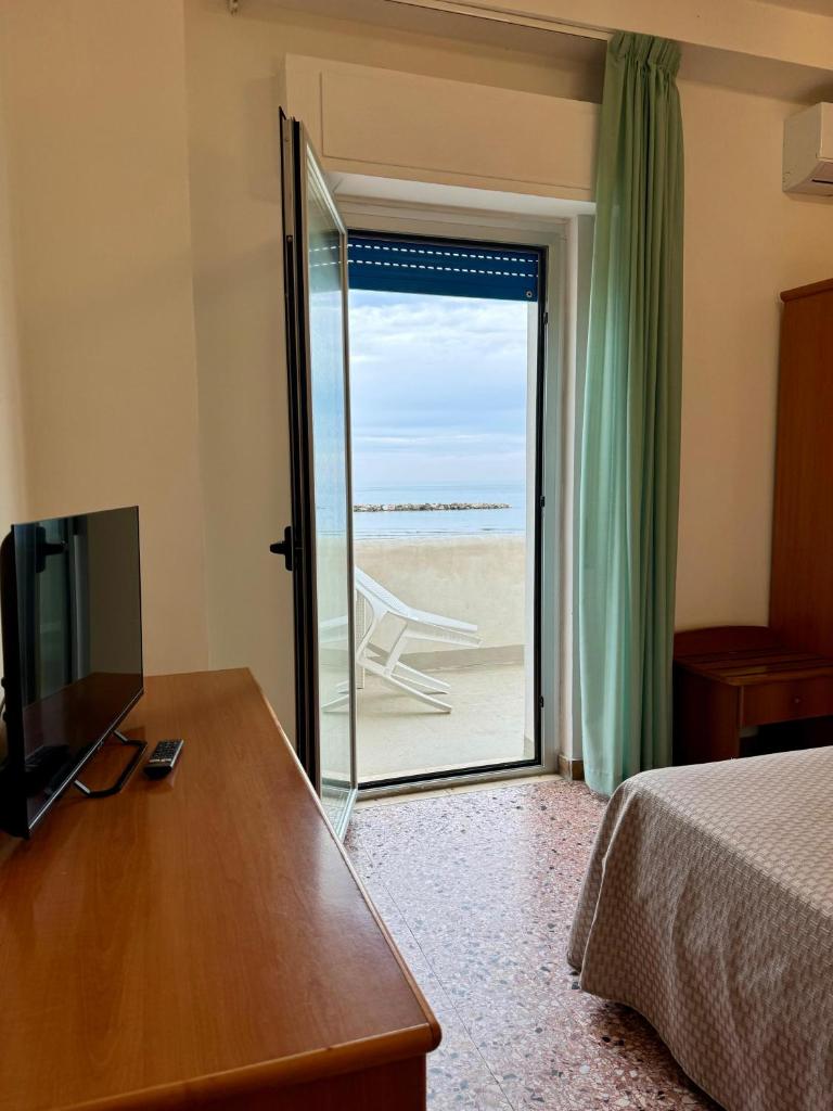 - une chambre avec un lit et une porte coulissante en verre menant à la plage dans l'établissement Hotel Valente, à Ortona
