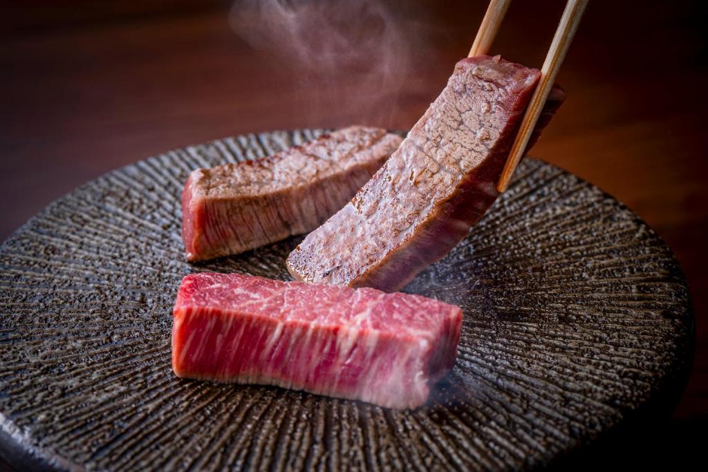 deux morceaux de viande sur une assiette avec deux baguettes dans l'établissement Okamotoya, à Beppu