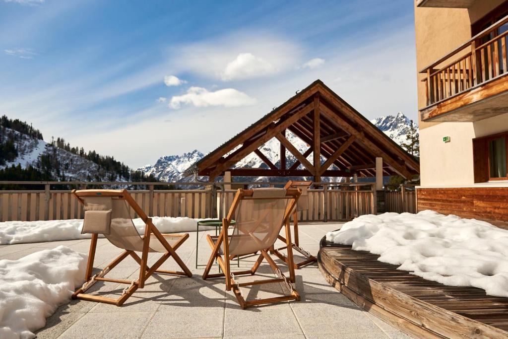 2 chaises et une table sur une terrasse enneigée dans l'établissement Villages Clubs du Soleil - OZ EN OISANS, à Oz