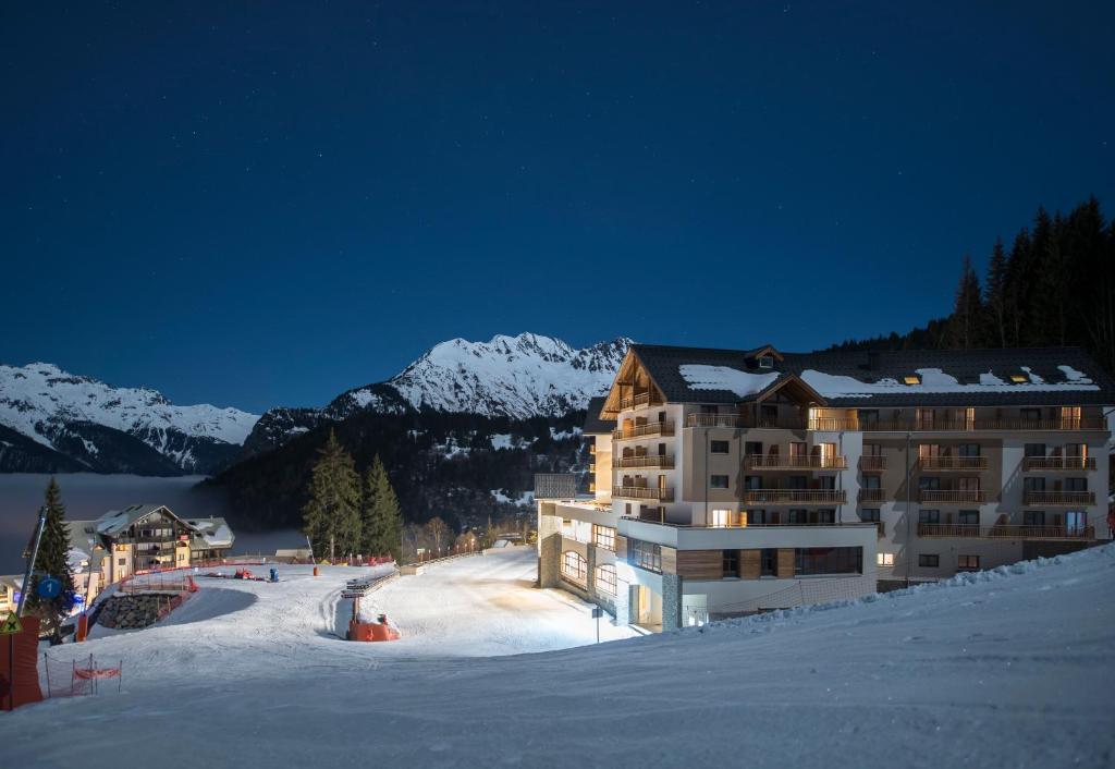 un bâtiment sur une piste de ski dans la neige la nuit dans l'établissement Villages Clubs du Soleil - OZ EN OISANS, à Oz