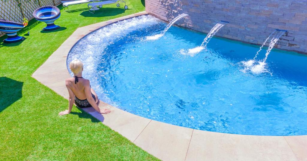 une personne assise sur l'herbe à côté d'une piscine dans l'établissement Hotel Torremaura, à Milano Marittima