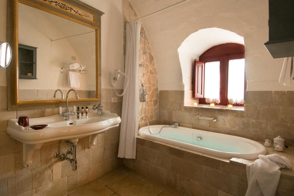 une salle de bain avec un lavabo, une baignoire et un miroir dans l'établissement Masseria Torre Coccaro, à Savelletri di Fasano