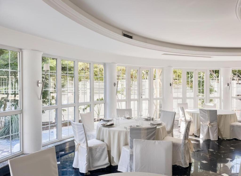 une salle à manger avec des tables et des chaises blanches et des fenêtres dans l'établissement Regent Beachotel, à Reggio de Calabre