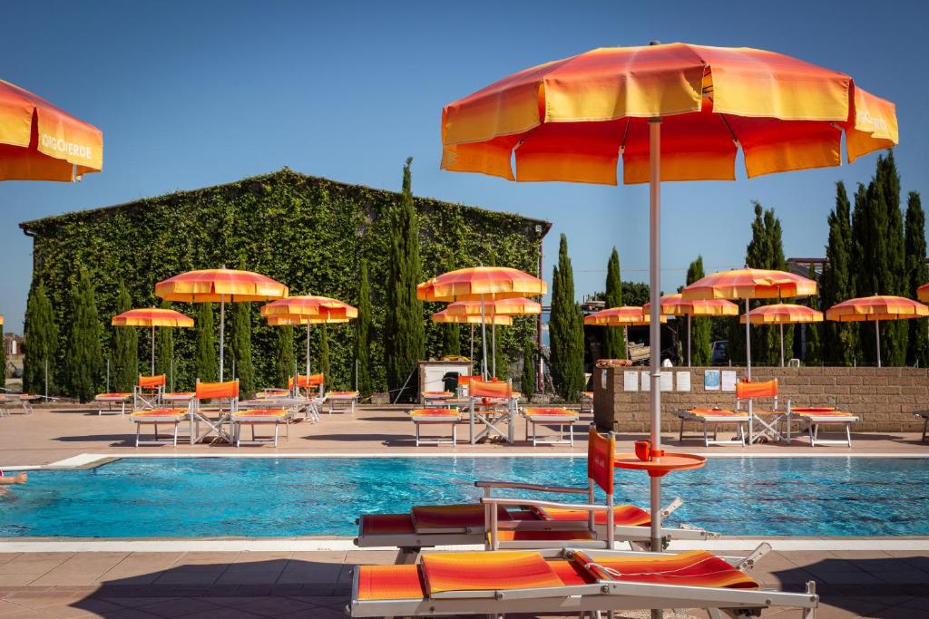 une piscine avec des chaises et des parasols orange et un groupe de tables dans l'établissement Hotiday Apartments Costa degli Etruschi, à Vada