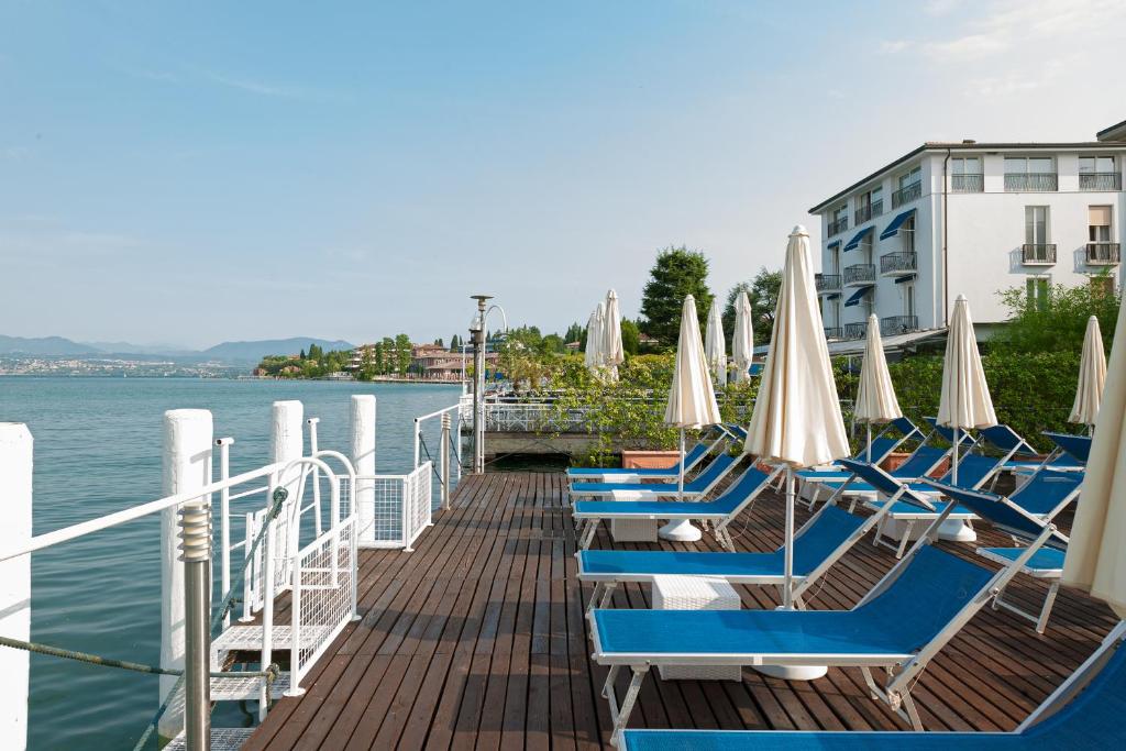 un quai avec des chaises et des parasols sur l'eau dans l'établissement Hotel Eden, à Sirmione