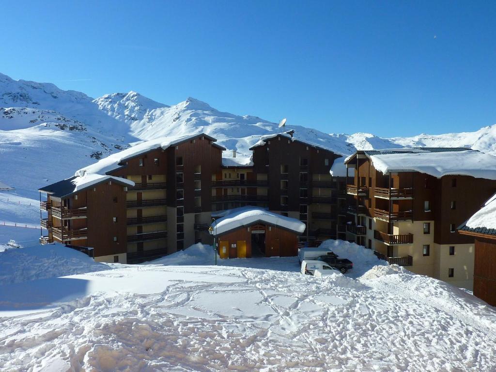 un bâtiment recouvert de neige avec des montagnes en arrière-plan dans l'établissement Reine Blanche Appartements VTI, à Val Thorens