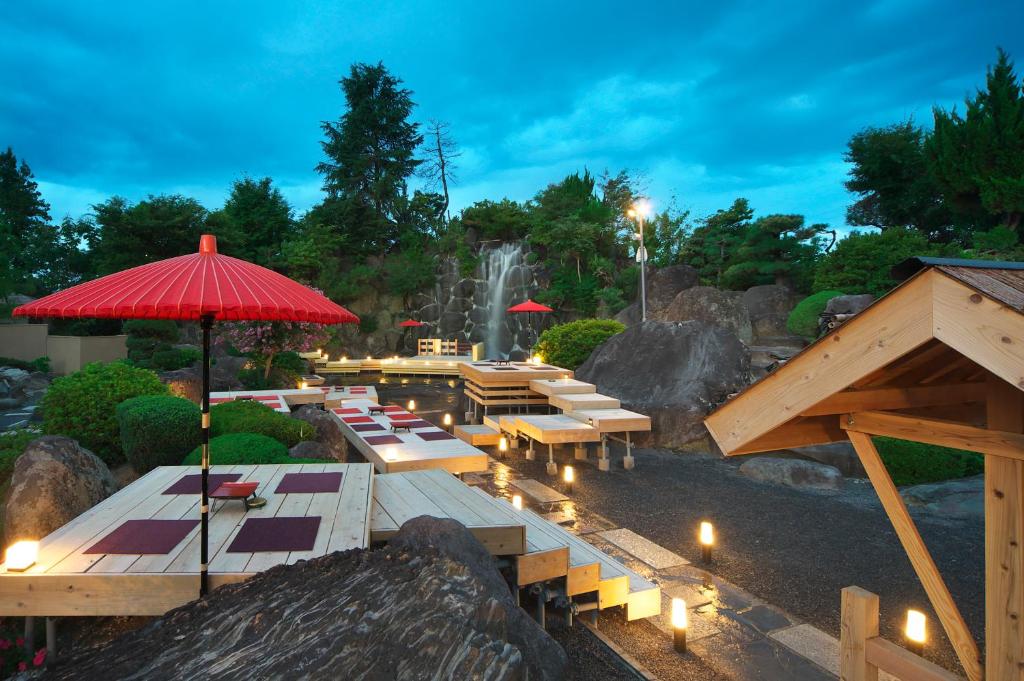 un restaurant avec des tables, des parasols et une cascade dans l'établissement Meitei no Yado Hotel Koshien, à Fuefuki