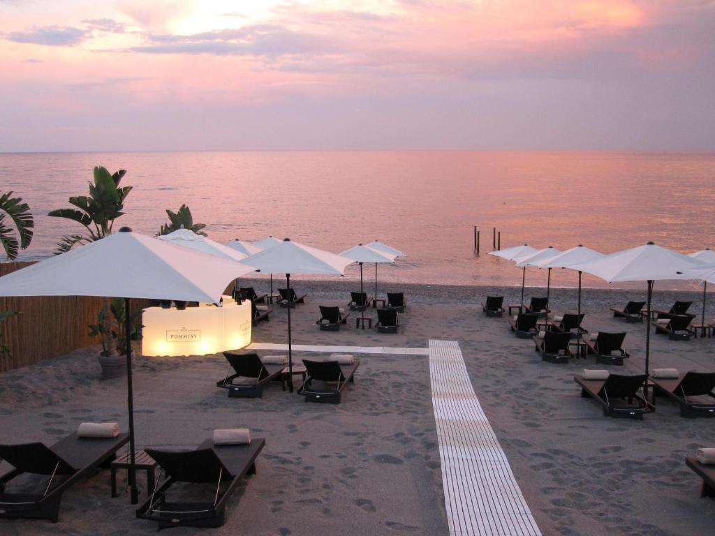 un groupe de chaises et de parasols sur une plage dans l'établissement Hotel Caparena, à Taormine