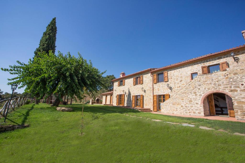 un grand bâtiment en pierre avec un arbre devant dans l'établissement Tenuta Angelici Winery Agriturismo Henni with pool sauna and jacuzzi Cortona, à Cortone
