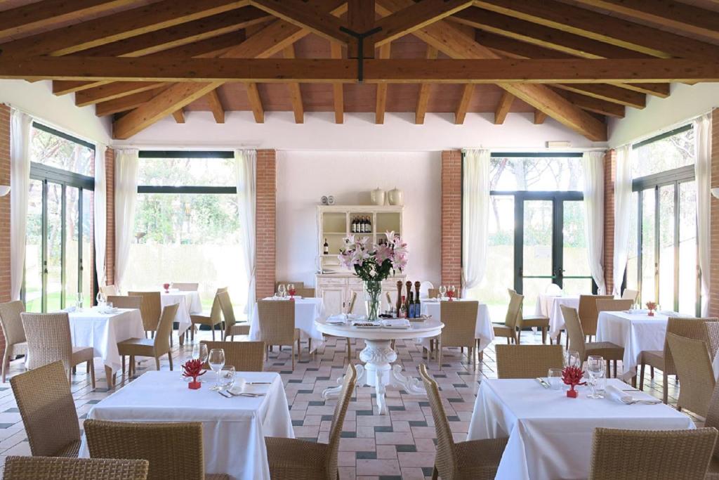 une salle à manger avec des tables et des chaises blanches et des fenêtres dans l'établissement Ricci Hotel - Marina di Grosseto, à Marina di Grosseto