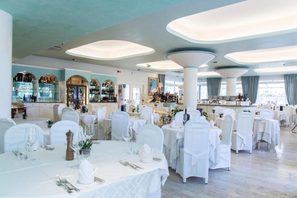 une salle à manger avec des tables blanches et des chaises blanches dans l'établissement Hotel Miramare, à Lignano Sabbiadoro