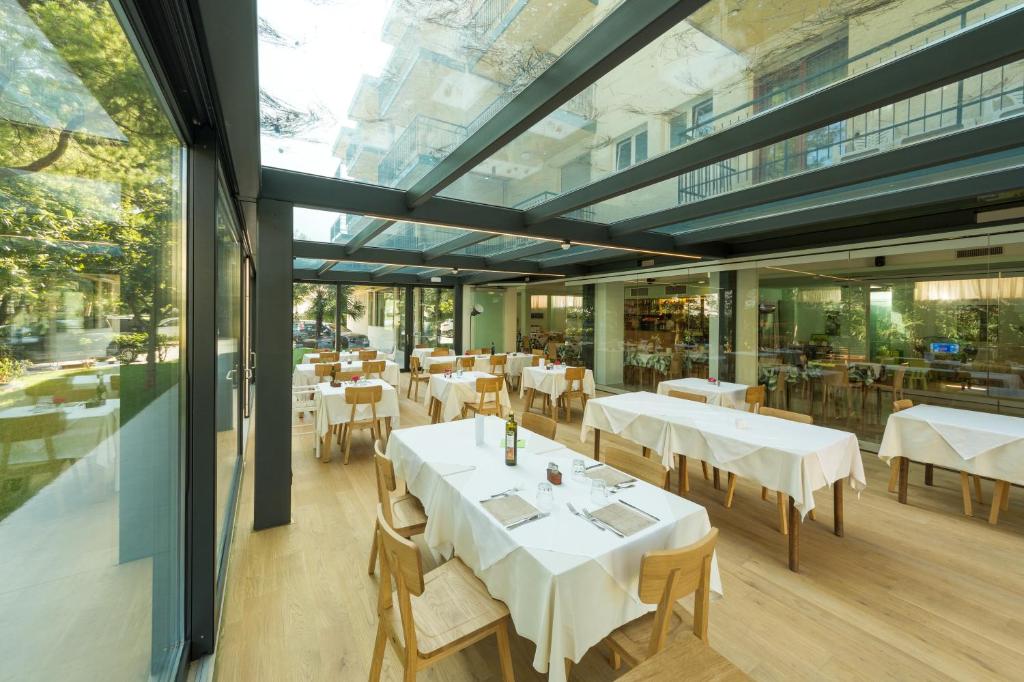 un restaurant avec des tables et des chaises blanches et des fenêtres dans l'établissement Hotel Adria, à Lignano Sabbiadoro