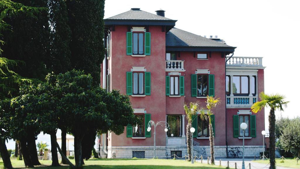 un grand bâtiment rouge avec des volets verts et des arbres dans l'établissement Villa Pioppi Hotel, à Sirmione
