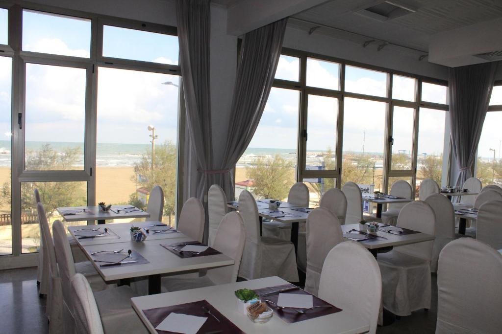 un restaurant avec des tables et des chaises blanches et des fenêtres dans l'établissement Hotel Universal, à Senigallia