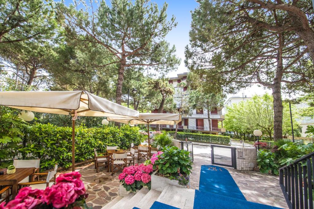 un patio avec des tables, des parasols et des fleurs dans l'établissement Renzo Hotel, à Cesenatico