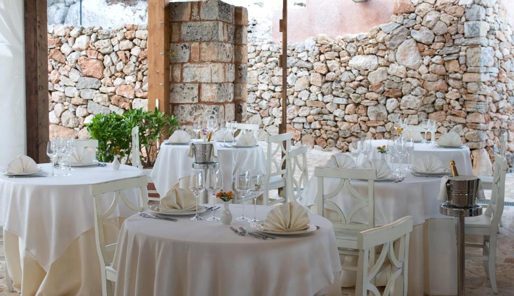 une salle à manger avec des tables et des chaises blanches et un mur en pierre dans l'établissement Antica Masseria Rottacapozza, à Torre San Giovanni 58 autres photos
