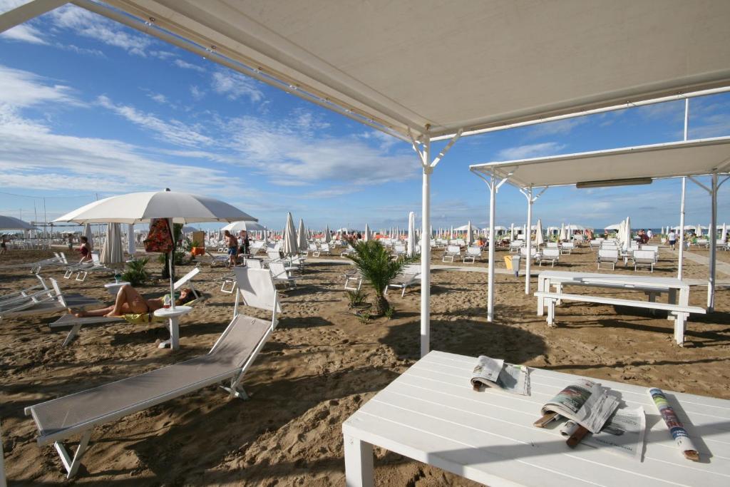 - une plage avec des chaises blanches, des tables et un parasol dans l'établissement Beach Hotel Clerice, à Rimini