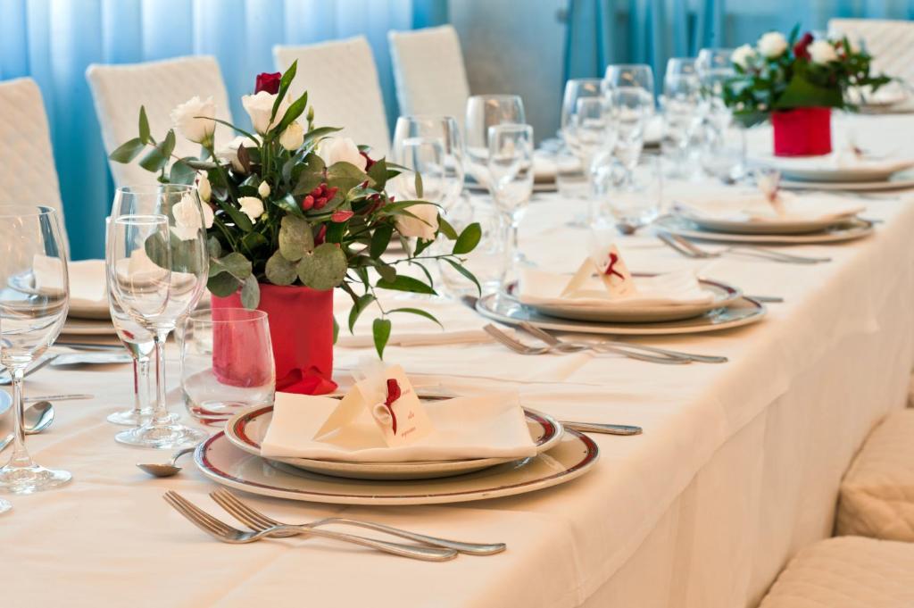 une longue table blanche avec des assiettes, des serviettes et des fleurs dans l'établissement Hotel Europa, à Cupra Marittima