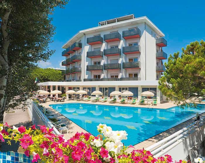 un hôtel avec une piscine bordée de parasols et de fleurs dans l'établissement Hotel Gimm, à Bibione