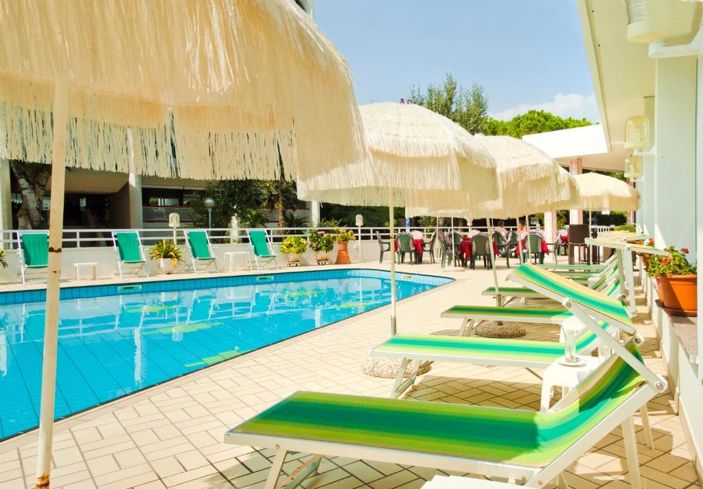 une piscine avec chaises longues et parasols dans l'établissement Hotel Gimm, à Bibione