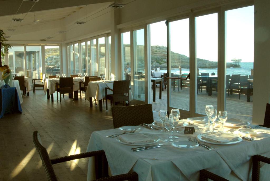 une salle à manger avec des tables et des chaises blanches et des fenêtres dans l'établissement Valtur Baia del Gusmay Beach Resort, à Peschici