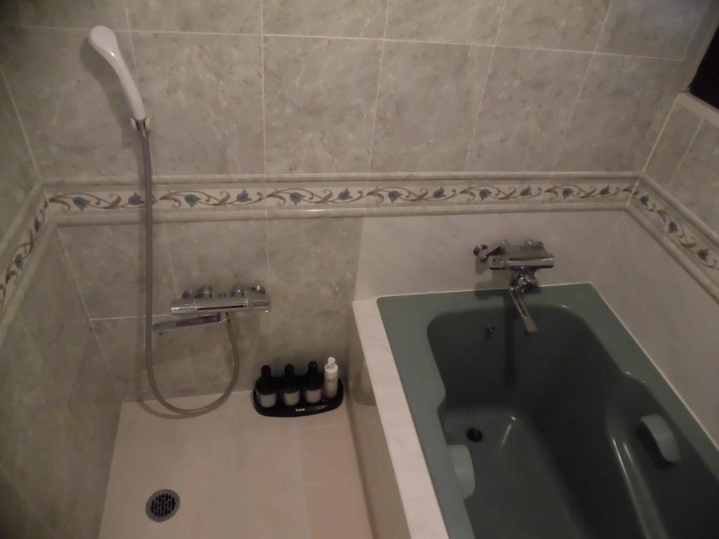 La salle de bains est pourvue d'une douche et d'une baignoire verte. dans l'établissement ホテル タイムレス 明石 男塾ホテルグループ, à Akashi