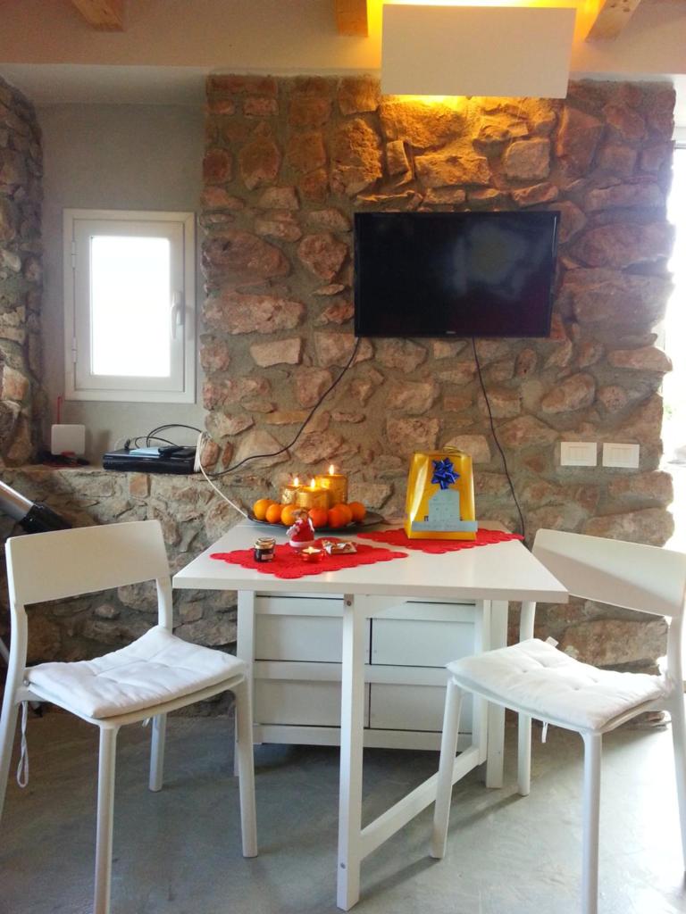 une table et des chaises blanches avec une télévision sur un mur en pierre dans l'établissement Andrea's Home, à Cefalù