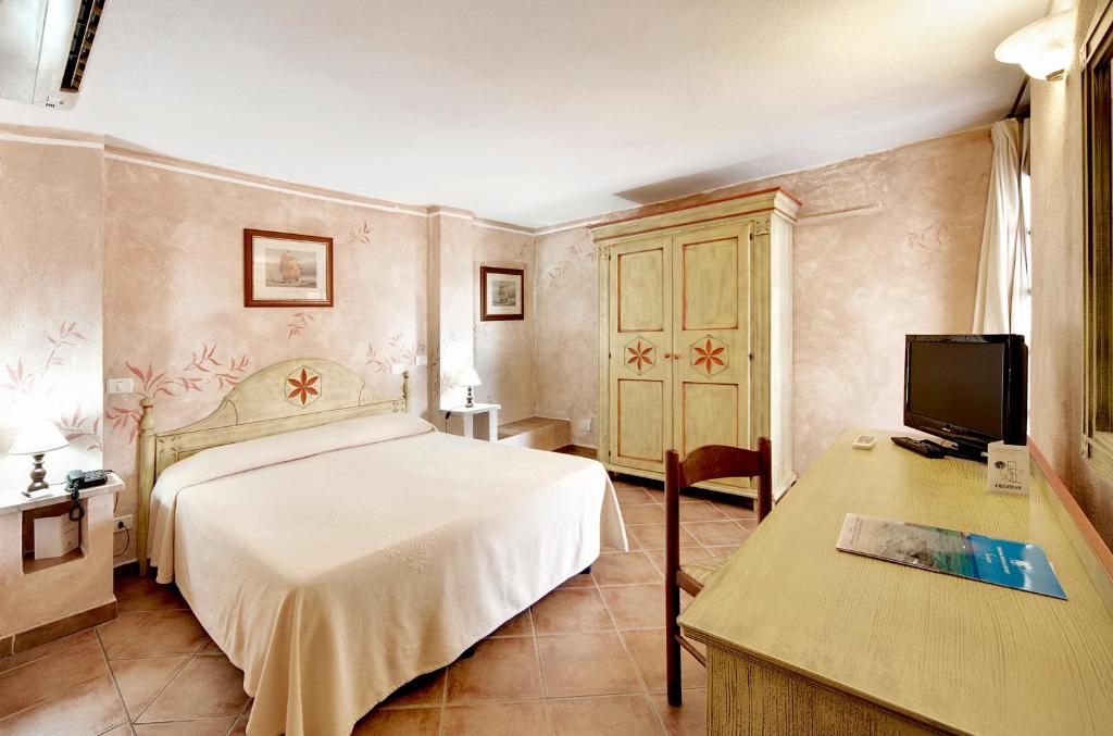 une chambre avec un lit et un bureau avec une télévision dans l'établissement Colonna Beach Hotel Marinella, à Marinella