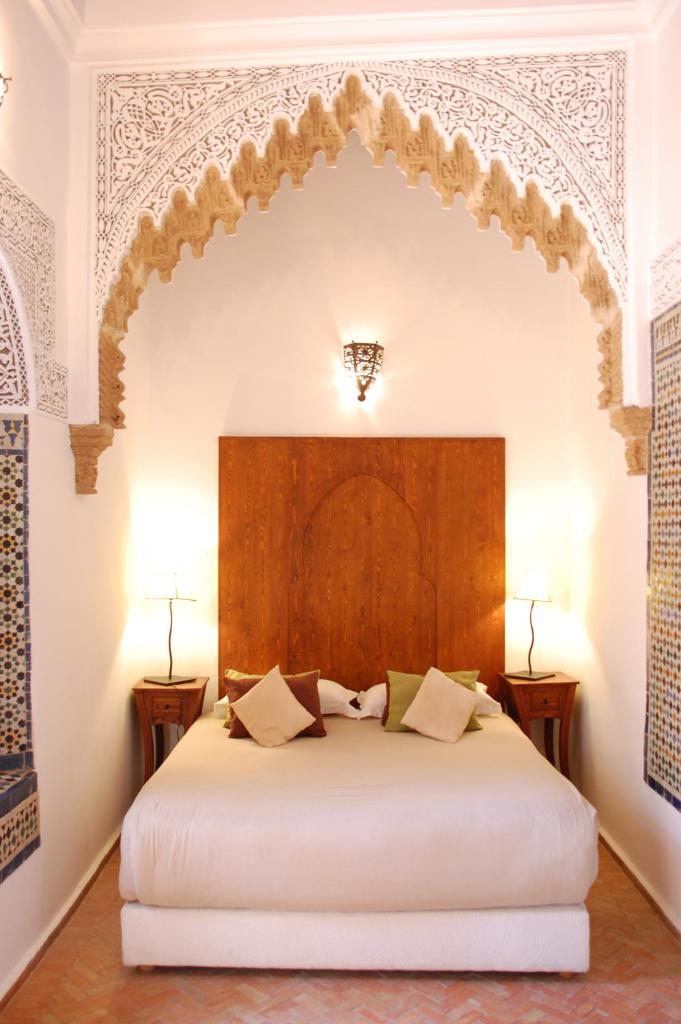 - une chambre avec un grand lit blanc et une tête de lit en bois dans l'établissement Riad Dar Soufa, à Rabat