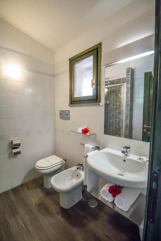 une salle de bain avec un lavabo, des toilettes et un miroir dans l'établissement Albaruja Hotel, à Costa Rei